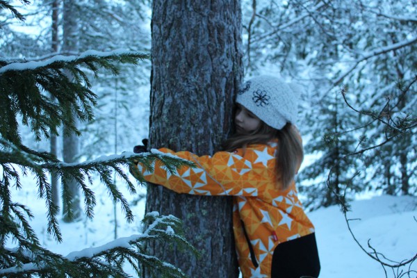 A girl hugging a tree in wintery forest.