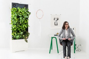 A woman sitting next to Naava's green wall.