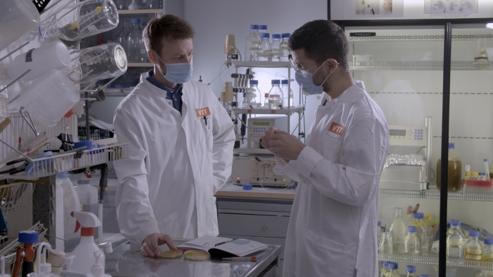 Two men in long white jackets discussing in a laboratory.