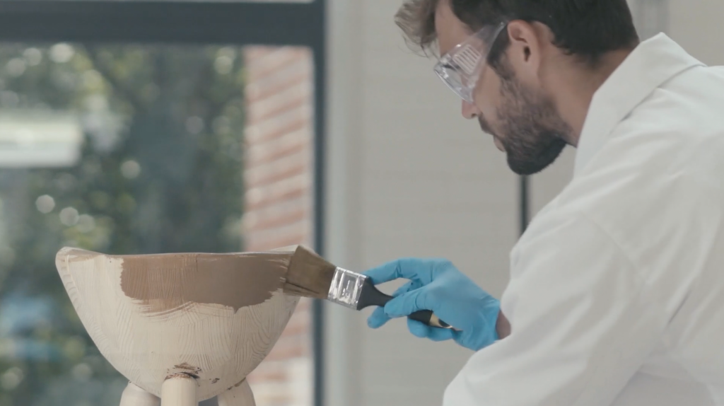 Man in a white laboratory coat is spreading lignin coating to a wood product.