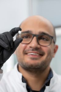 Male researcher with glasses showing a white dental implant crowns nanocomposite between his thumb and index finger.