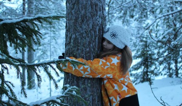 A girl hugging a tree in wintery forest.