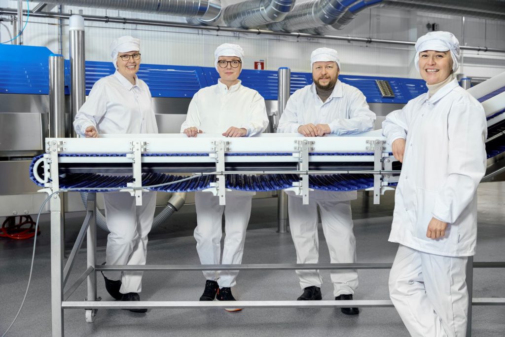 Four people stand in the production facility in white protective suits and hats. 